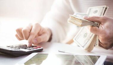 A close-up of two hands, one using a calculator and the other holding a stack of money.