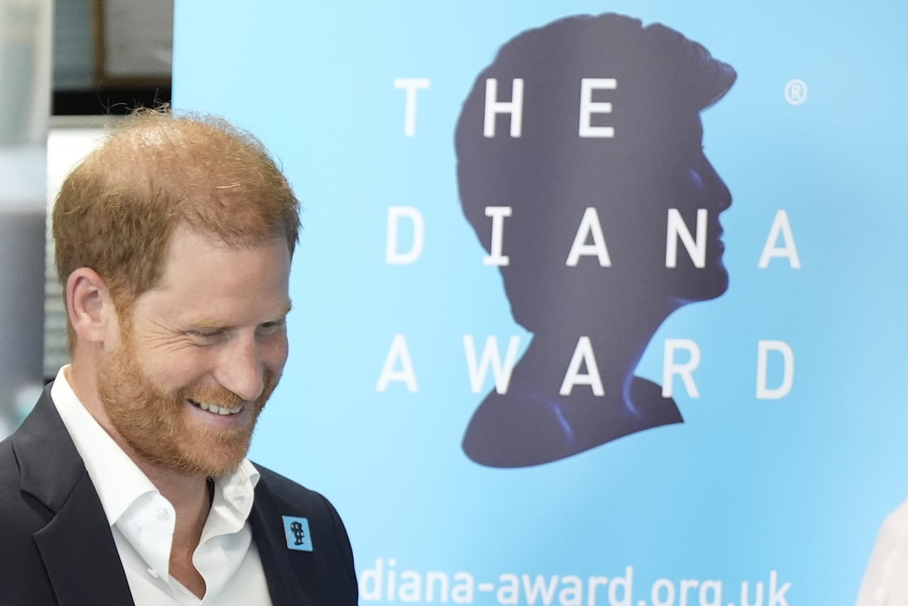 A person looks down as they stand beside a sign that shows the silhouette of a head and the words 'The Diana Award.'