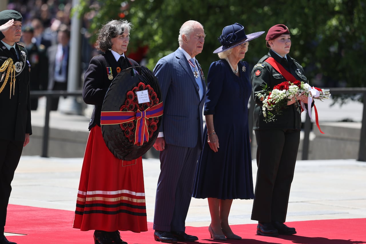 People stand in a line holding wreaths on a red carpet.