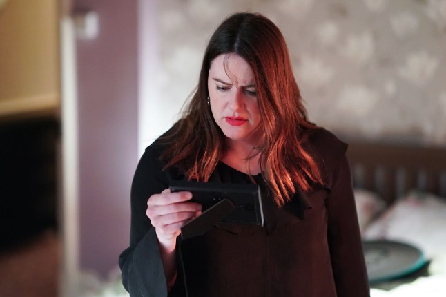 Zoe looking worried while holding a photo frame in EastEnders
