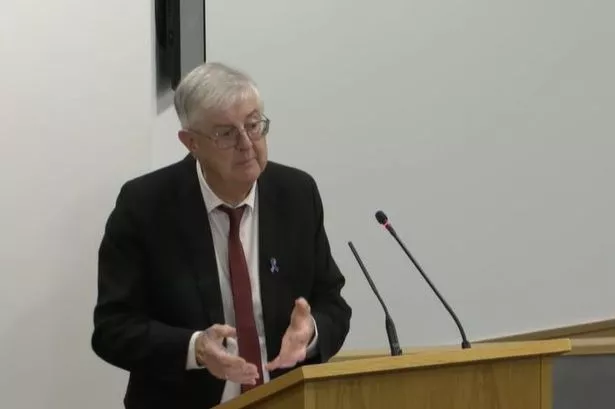 Mark Drakeford in a suit stood in front of a podium