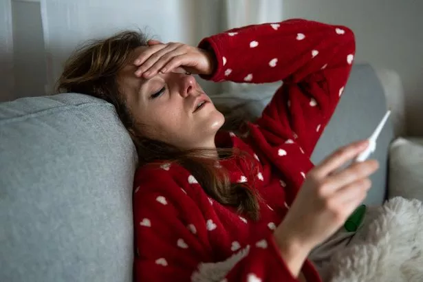 Sick woman suffering from cold and flu, measuring her body temperature while lying on a sofa