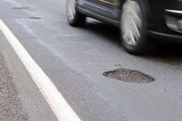 Car drives past a pothole.