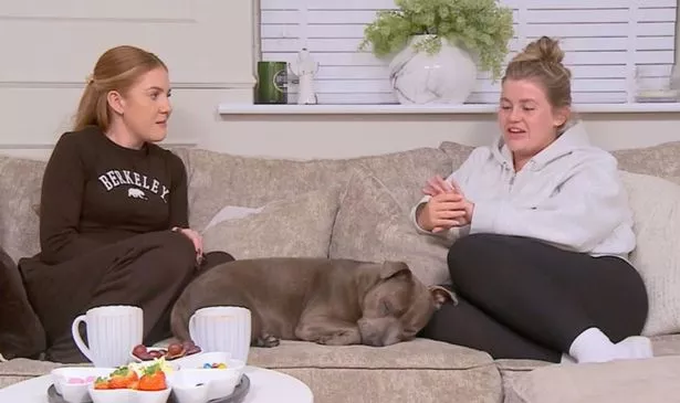 Two women sat on the sofa as one looks at her engagement ring