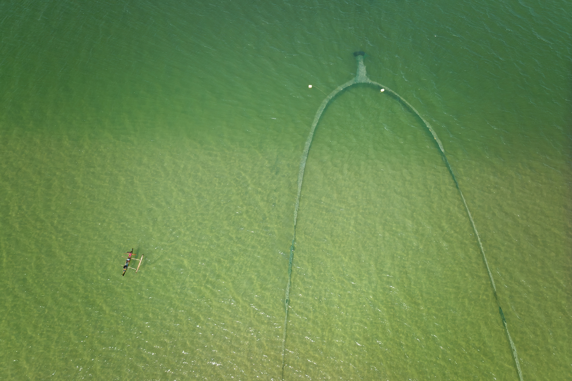 Aerial image of a large beach seine, with a small boat in the water nearby.