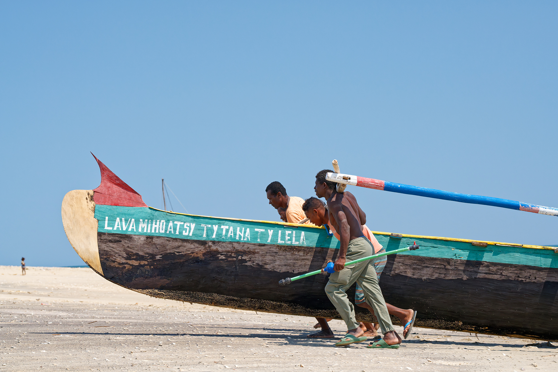 Fishermen haul a long, narrow boat onshore.
