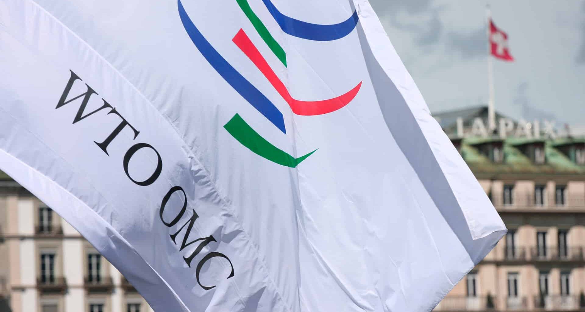 White flag with the logo of the World Trade Organisation (WTO) at its headquarters in Generva (Switzerland). The building has the the word “La Paix” on the roof and a Swiss flag flying.