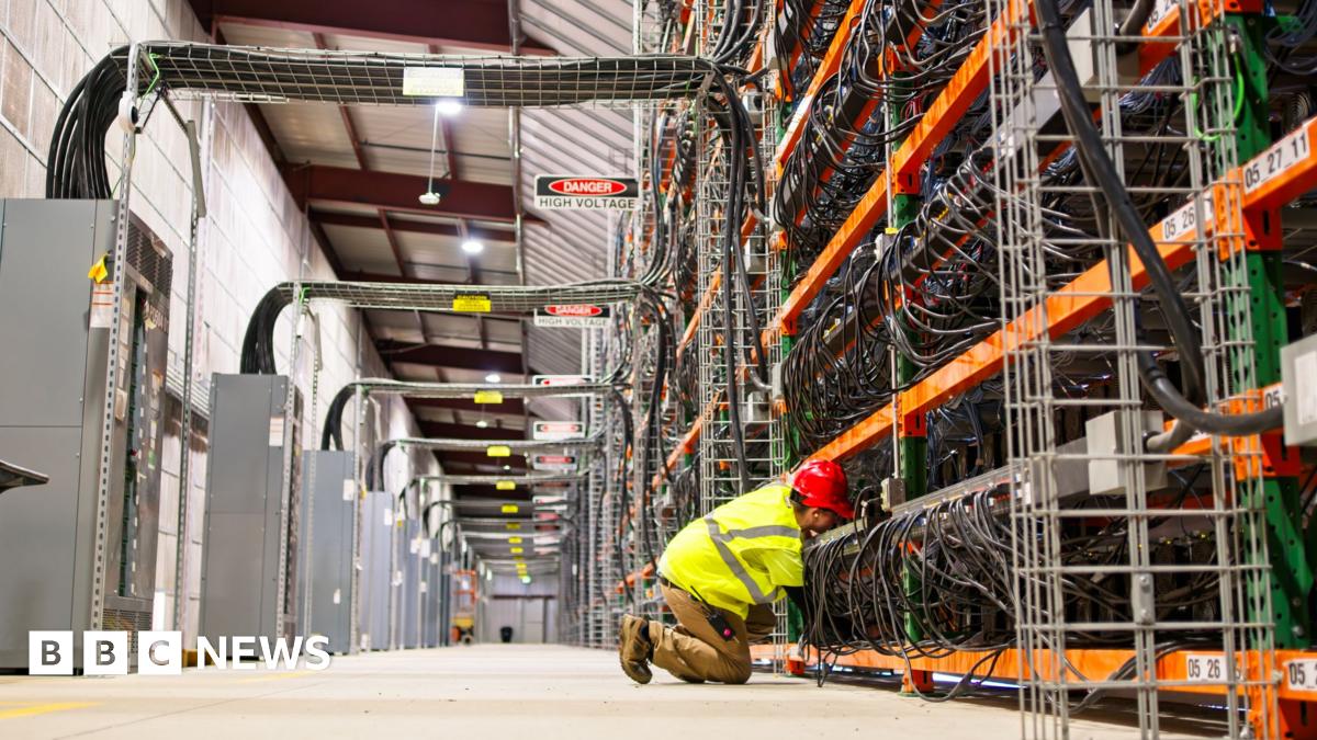 A technician wearing PPE working on racks of equipment in a data center for cryptocurrency mining, cloud services and AI computing in a large, temperature controlled warehouse in a remote location in Stutsman County, North Dakota.