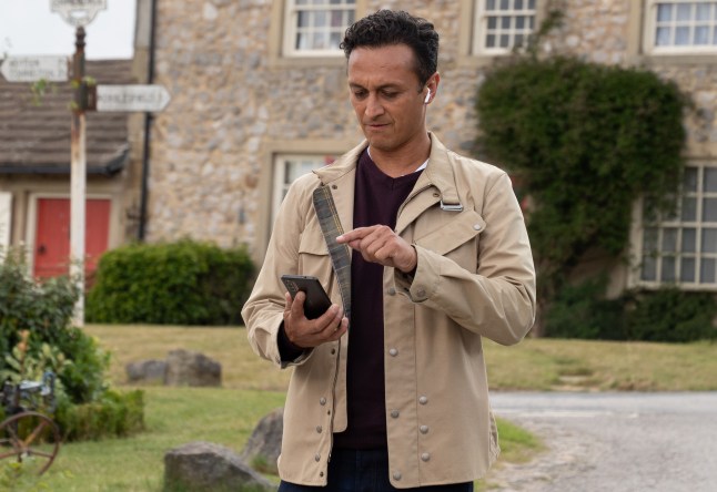 Jai texting while walking down Main Street in Emmerdale