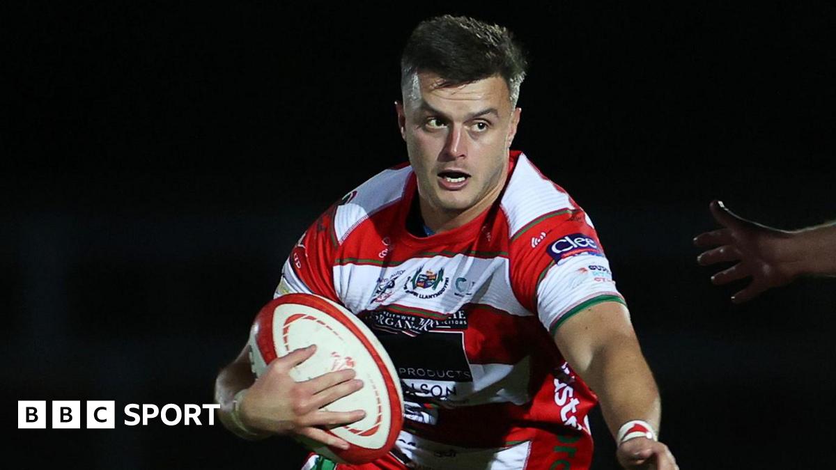 Ioan Hughes holds a rugby ball wearing a red and white hooped jersey