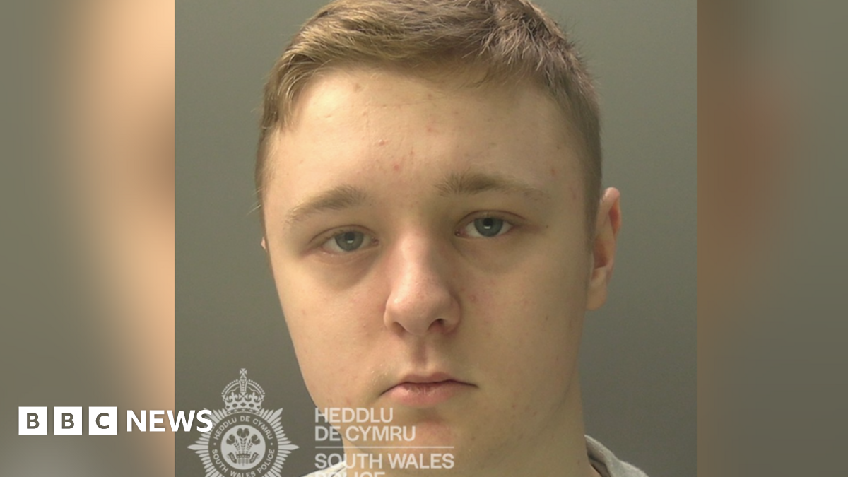 Custody image of Cory Jones. He has short blonde hair and a serious look. In the bottom left corner there is the logo for South Wales Police.