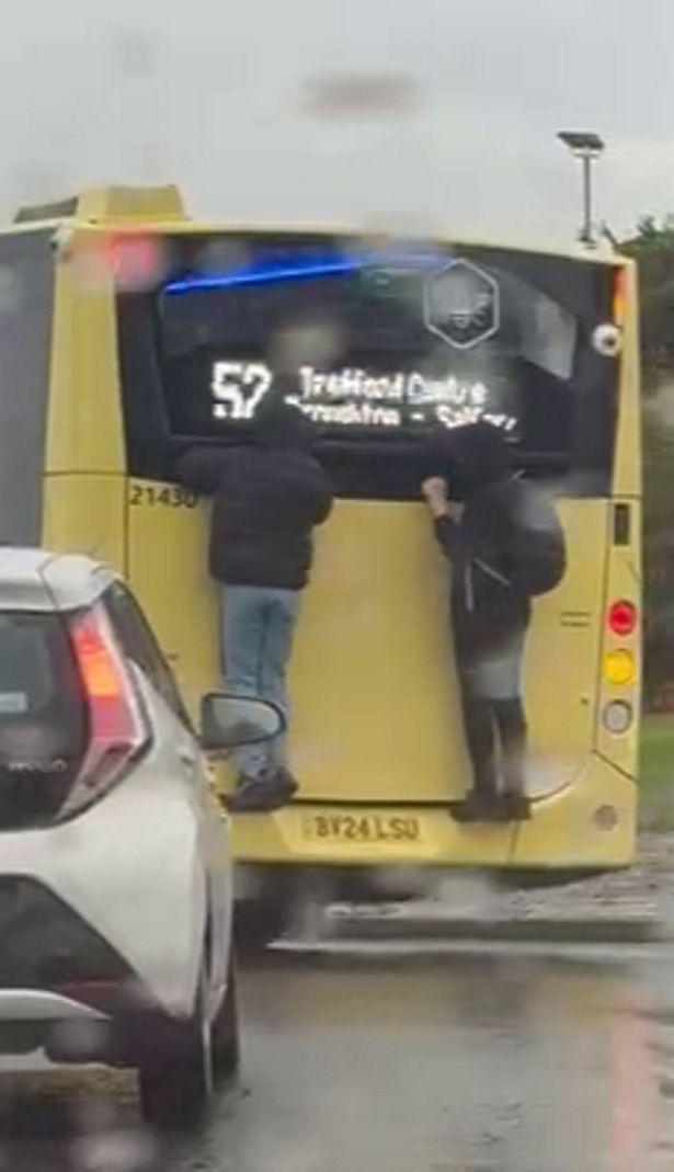 Two teenagers clinging onto the back of a bus near the Trafford Centre, in Manchester. // Shocking video footage shows two teenagers clinging onto the back of a bus on a busy main road. The horror footage - which was filmed on a shocked member of the public's phone - captures the two boys hanging off the back of a Bee Network bus near the Trafford Centre, in Manchester, yesterday (Oct 19). The teenagers - both dressed in black coats - had climbed onto the back of a 52 service which travels from Failsworth to Trafford. The 12 clip was filmed at the Ellesmere Circle roundabout as the bus made its way down Redclyffe Road.