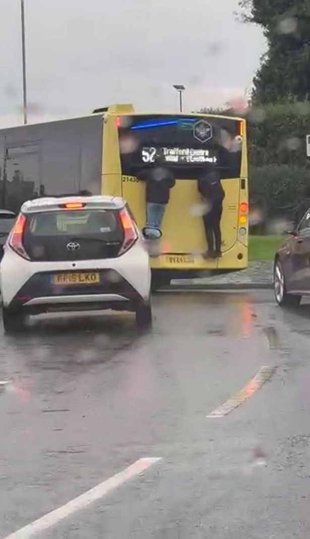 Two teenagers clinging onto the back of a bus near the Trafford Centre, in Manchester. // Shocking video footage shows two teenagers clinging onto the back of a bus on a busy main road. The horror footage - which was filmed on a shocked member of the public's phone - captures the two boys hanging off the back of a Bee Network bus near the Trafford Centre, in Manchester, yesterday (Oct 19). The teenagers - both dressed in black coats - had climbed onto the back of a 52 service which travels from Failsworth to Trafford. The 12 clip was filmed at the Ellesmere Circle roundabout as the bus made its way down Redclyffe Road.
