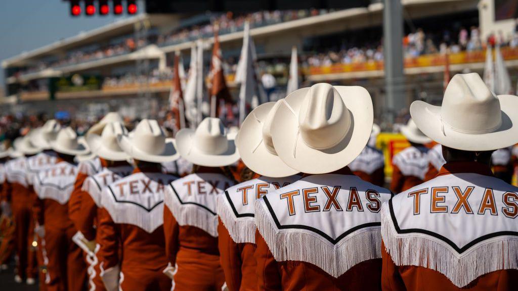 The Texas Longhorns band, wearing shirts with 'Texas' on the back and cowboy hats, on the track before the United States Grand Prix in 2024
