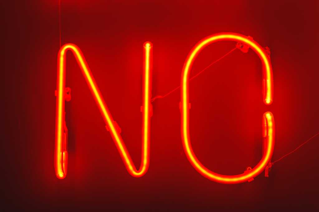 Red neon NO sign on a dark background. Sign says no in bright red narrow capital letters.
