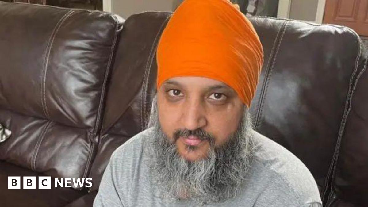 Paramjit Singh wearing an orange turban and grey shirt is sitting on a brown sofa.