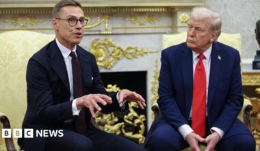 Alexander Stubb on left wears a dark suit, white shirt and dark purple tie, with glasses. He is speaking, his hands up for emphasis. On the right, Donald Trump is wearing a blue suit, white shirt and red tie, as he listens.