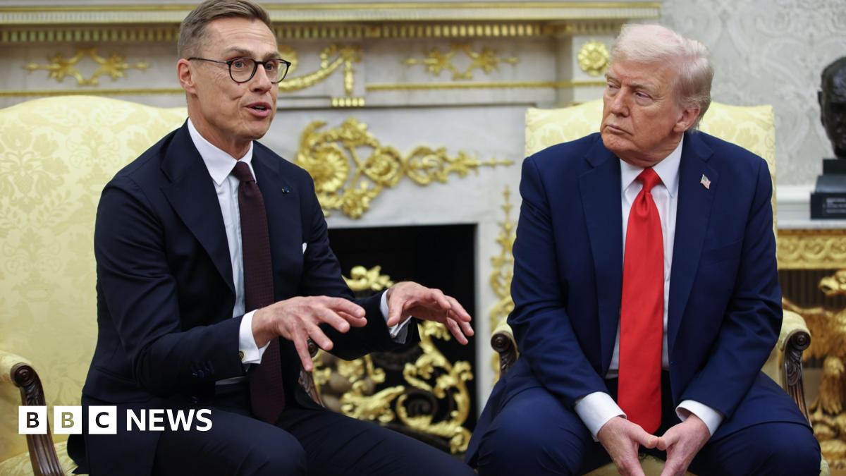 Alexander Stubb on left wears a dark suit, white shirt and dark purple tie, with glasses. He is speaking, his hands up for emphasis. On the right, Donald Trump is wearing a blue suit, white shirt and red tie, as he listens.