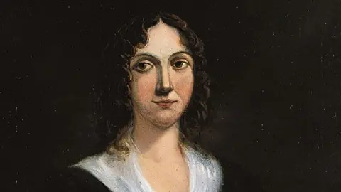 Suffolk County Council A painting depicting Margaret Catchpole. It shows the head and shoulders of a woman with shoulder length wavy dark hair and large brown eyes. She is wearing a black top with a white shawl collar and is seen against a dark background