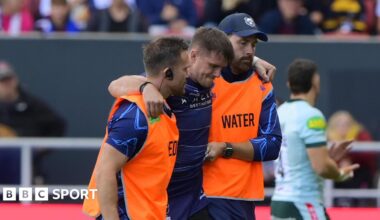 AJ MacGinty being helped off the pitch by two Bristol staff members