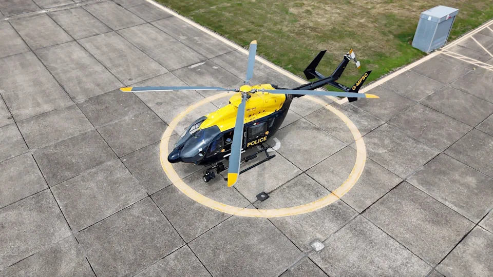 An aerial view of a police helicopter on its helipad in Essex. There's a large yellow landing circle painted underneath the helicopter on the concrete
