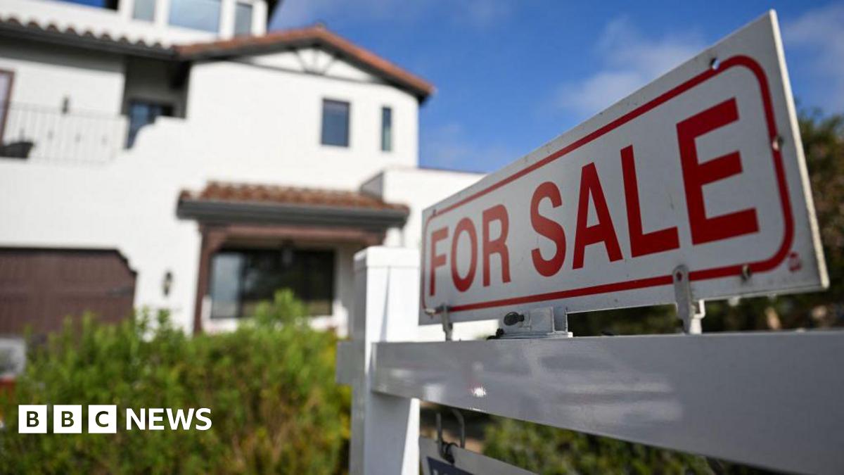 A white sign reading 'for sale' in red letters hangs in front of a white house.