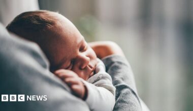 A baby lies asleep in its carers arms.