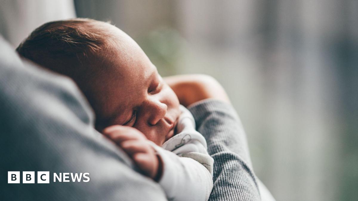 A baby lies asleep in its carers arms.
