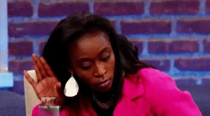 Person in pink jacket playfully holds hand to ear, gesturing to listen