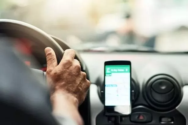 An image of a person's hands on the steering wheel of a car, with a phone in a holder showing a map.