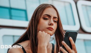 A young woman, looking concerned, looks at here smartphone.