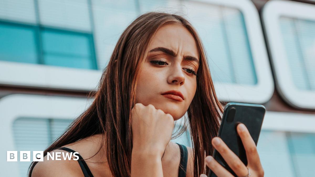 A young woman, looking concerned, looks at here smartphone.