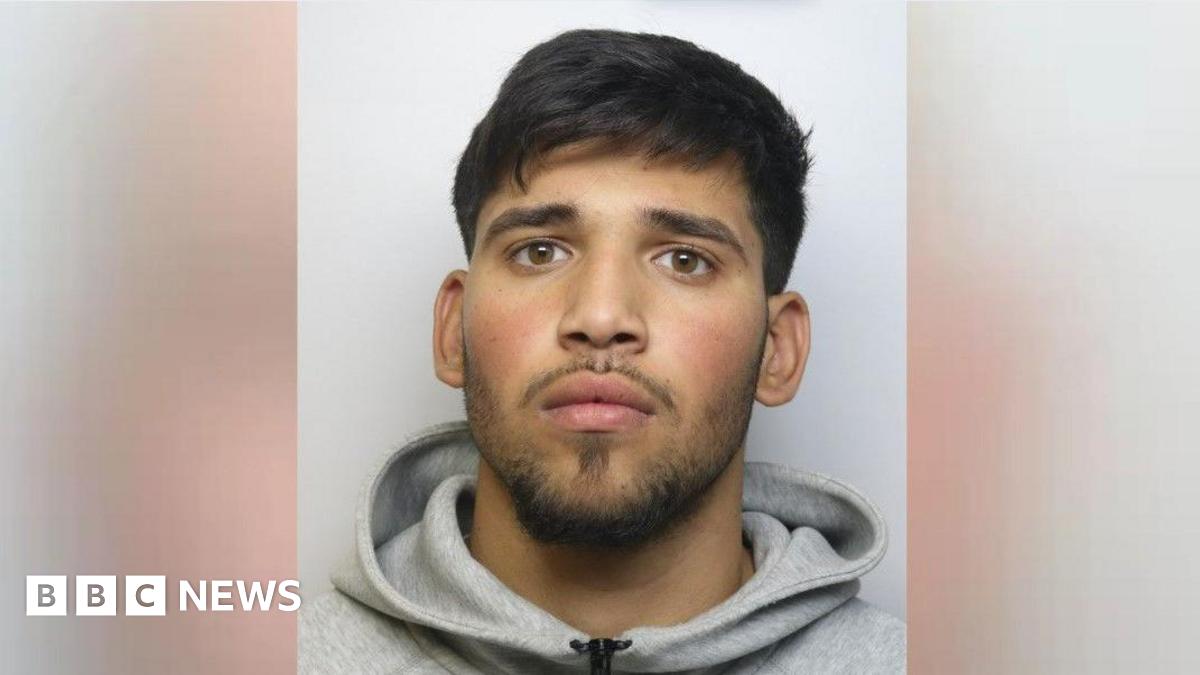 Alex Tiuga is staring at the camera. He has short black hair and a short trimmed beard and moustache and is wearing a grey hoody