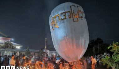 People lighting candles in the night time around a giant white balloon
