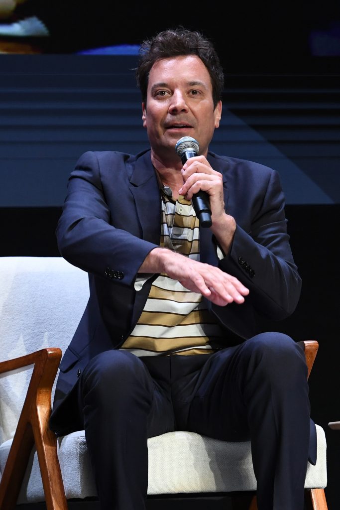 Jimmy Fallon at an event with microphone sitting down 