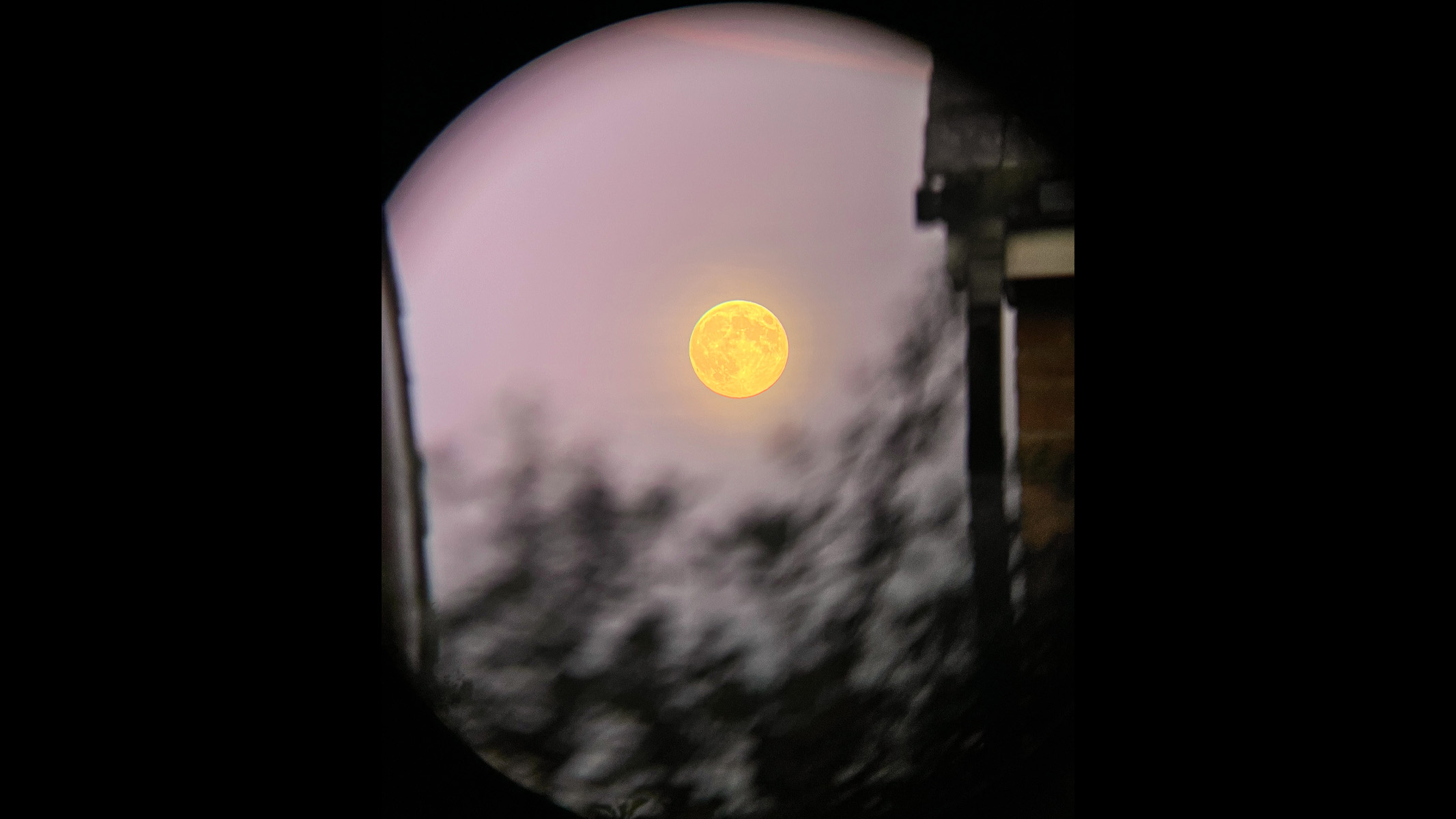 full beaver moon rising in a pink sky through binoculars