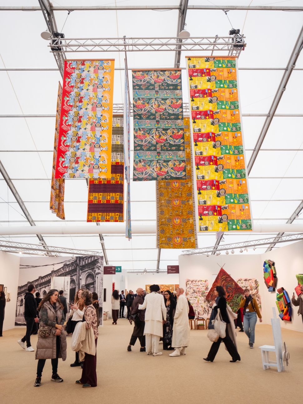 Colorful patterned textile banners hanging from the ceiling in the “Echoes in the Present” section, with visitors walking through the booth below.