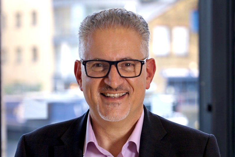 Portrait of Eric van der Kleij wearing a pink shirt, black blazer, and glasses.