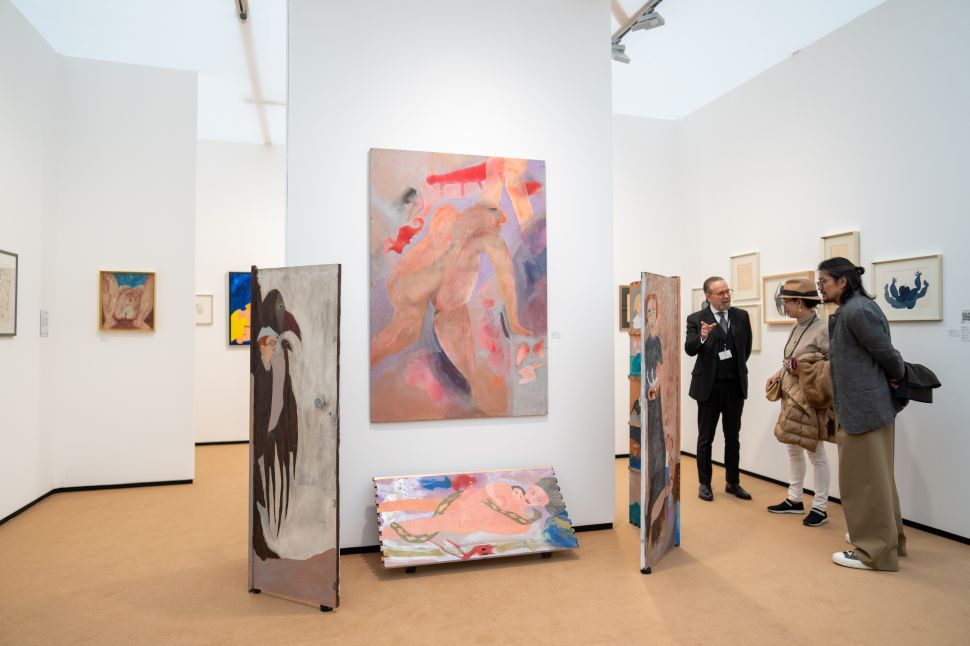Installation view at Frieze Masters 2025 featuring expressive figurative paintings by a modernist artist, including a large central nude composition and painted doors arranged as freestanding panels, with additional drawings and works on paper on the surrounding walls as visitors engage with a gallerist.