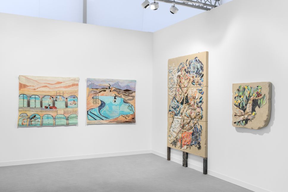Installation view of a booth at Frieze London 2025 featuring textile and relief works: two pastel-colored woven tapestries depicting swimmers and architectural pools hang on the left wall, while on the right wall two sculptural wall pieces made of layered, painted fragments create dynamic figurative and botanical forms.