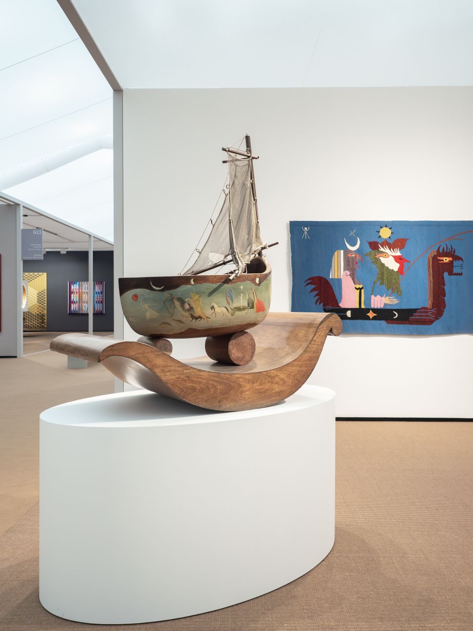 Booth featuring a wall covered in floral-patterned wallpaper with a totem-like sculptural figure at the center, and an abstract blue hide-shaped artwork on the side wall.