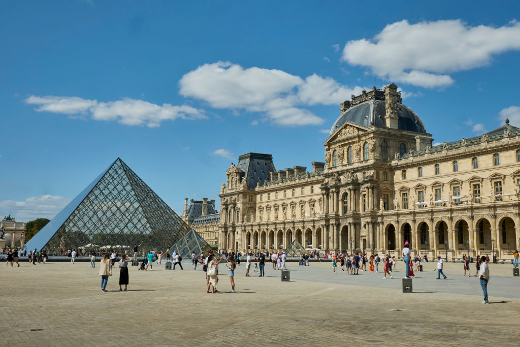 A triangular shaped glass building next to a larger, classical stone building.