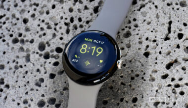 A Google Pixel Watch rests on a lava rock displaying the Utility watch face with a Fitbit shortcut.