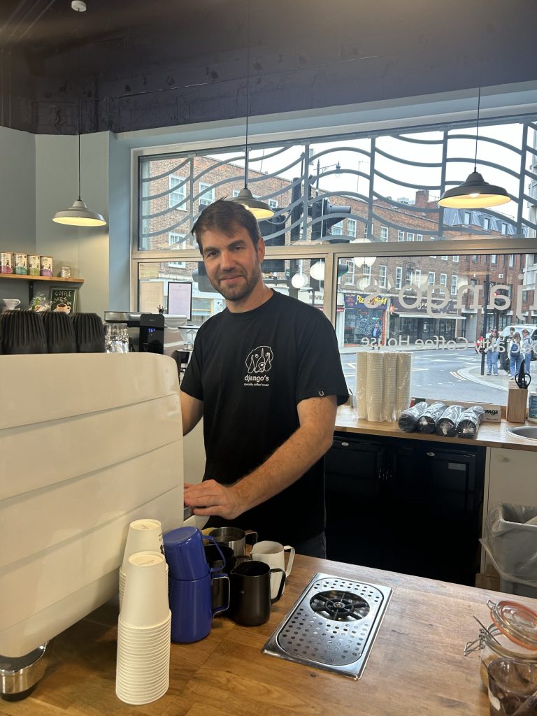 A man poses behind a coffee machine in a cafe