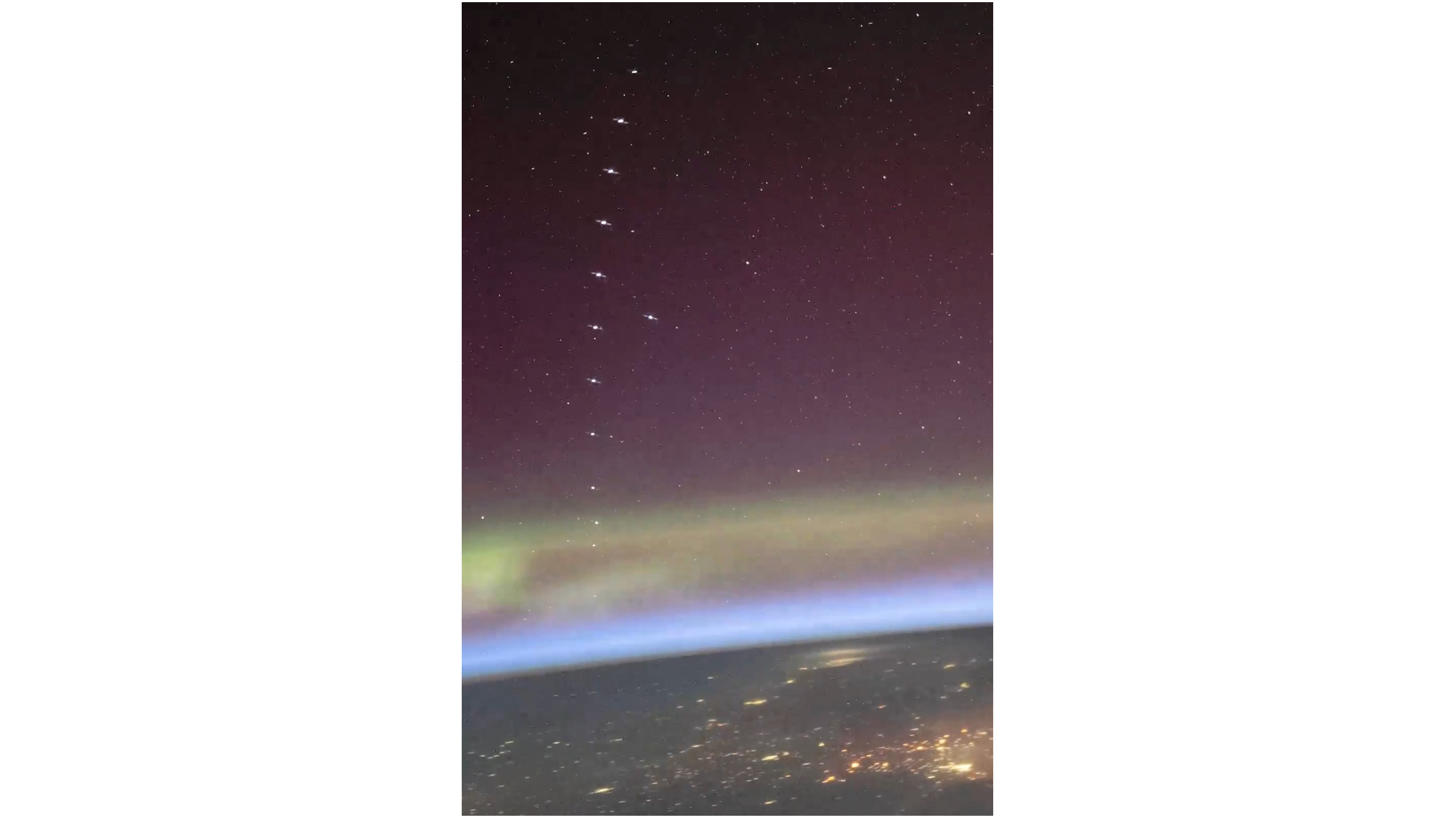 image of a dozen of so satellites in a row above the greenish northern lights, as seen from the space station