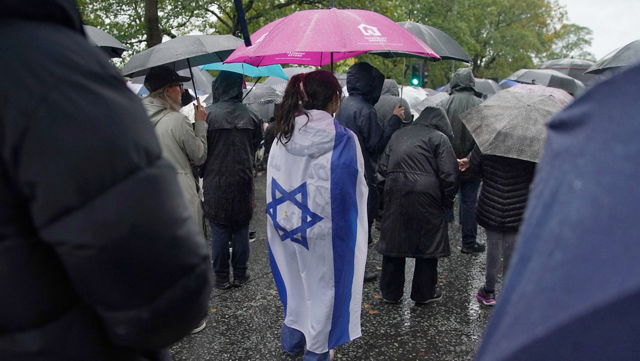 A woman wears the flag of Israel wrapped over her back as she attends a vigil for the victims of the attack on at Heaton Park Hebrew Congregation synagogue, in Crumpsall, Manchester, England, Friday, Oct. 3, 2025. (AP Photo/Ian Hodgson)