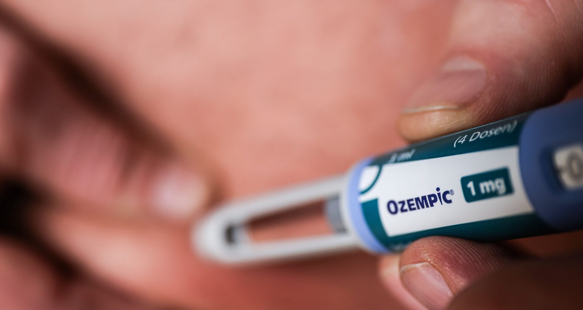 A closeup of a person using a pen-style syringe to inject Ozempic. The syringe is in focus in the foreground.