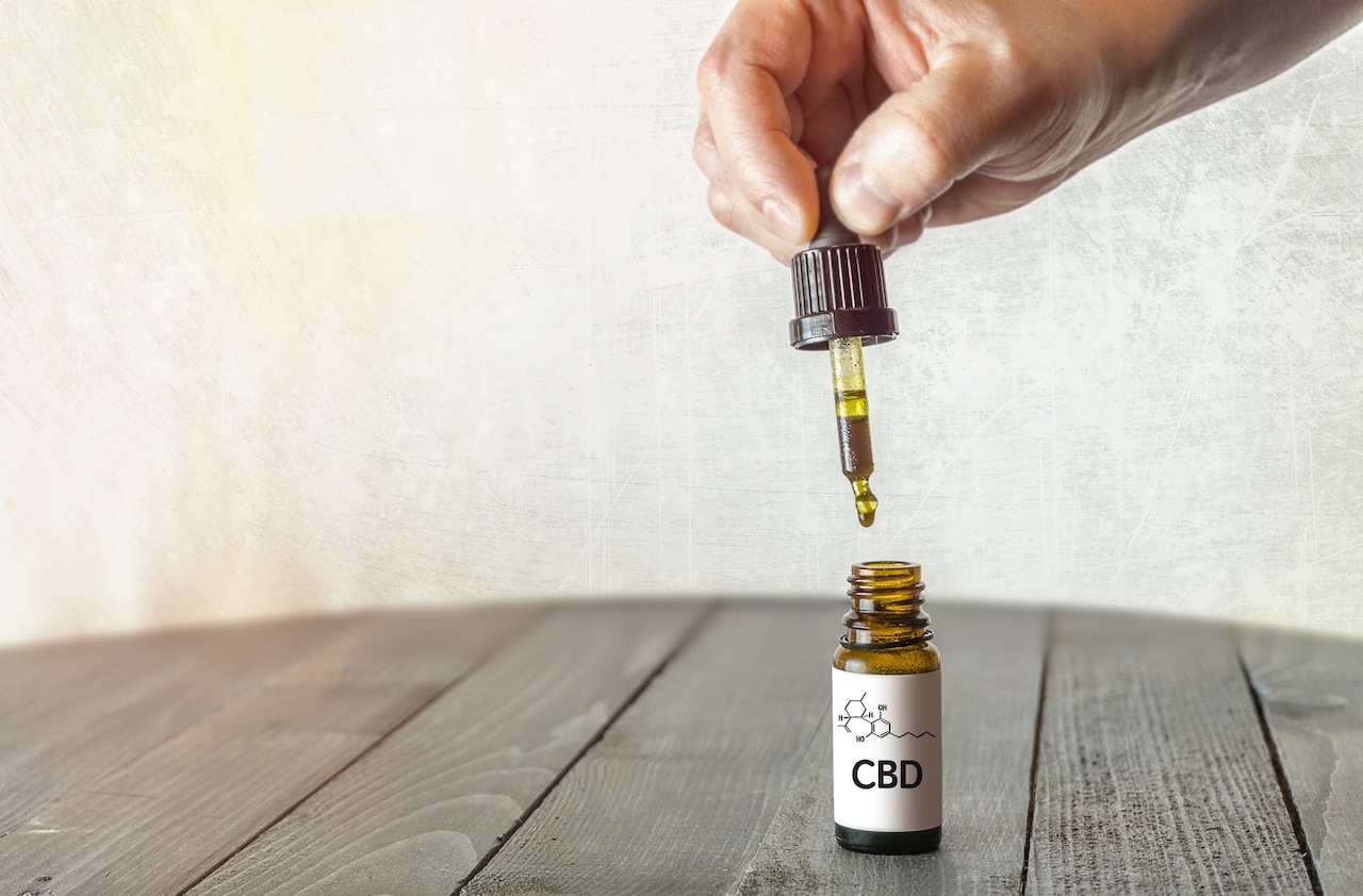 A hand holds a dropper above a bottle of CBD oil