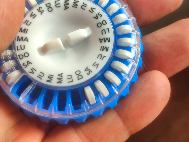 A human hand holding a daily pill dispenser for hormone therapy