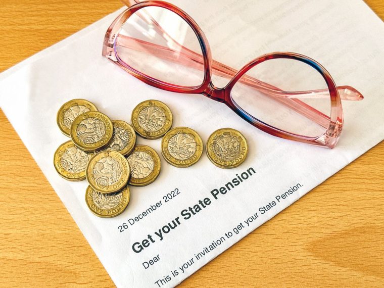 Offical letter telling a person of state retirement age in the UK they can get their pension, with one pound coins and a pair of reading glasses.